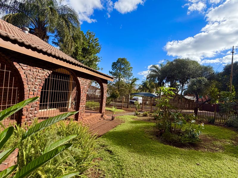 Front view of a face brick house featuring an arched veranda, security bars, and a well-maintained garden with perimeter fencing.