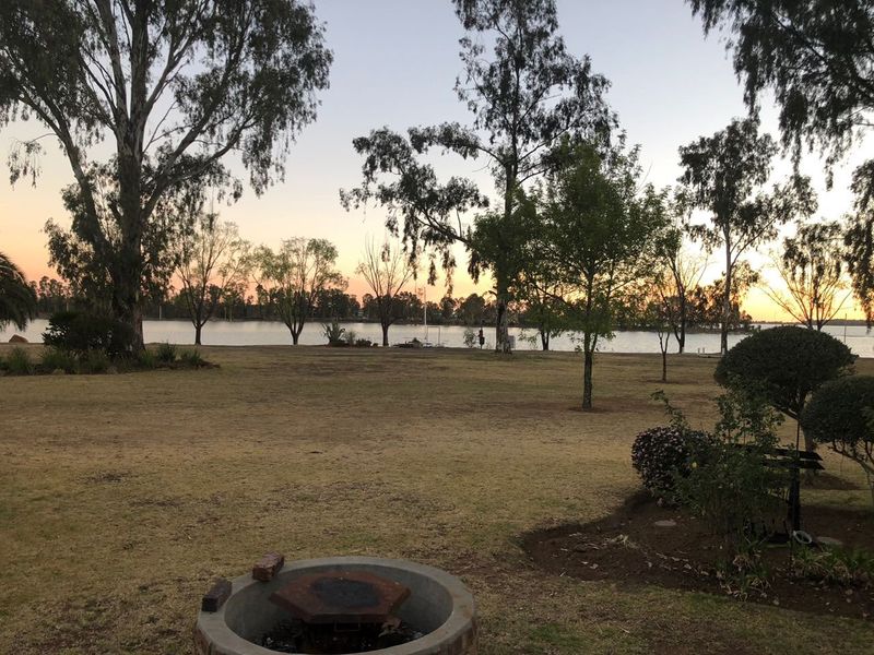 A scenic view of the waterfront garden at sunset, featuring a built-in fire pit and mature trees.