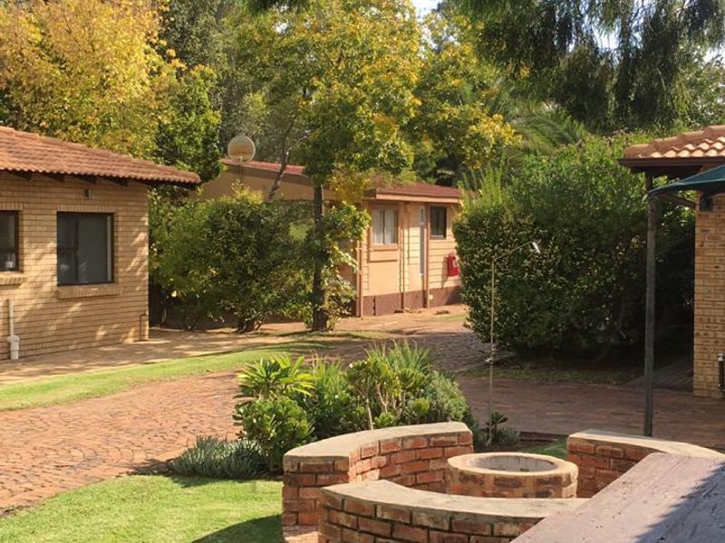 A covered patio area featuring a built-in brick fire pit, overlooking a landscaped garden and paved courtyard between residential buildings.