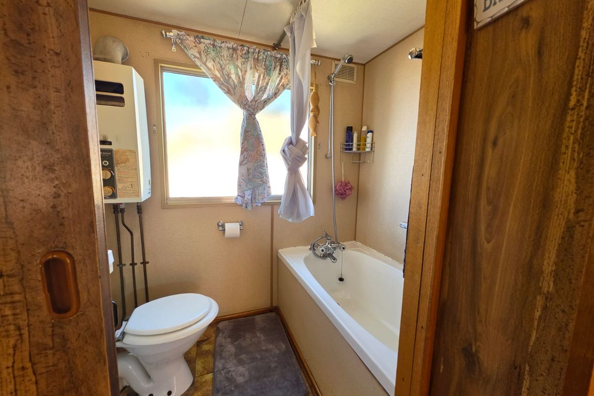 Compact bathroom featuring a bathtub with shower mixer, toilet, and wall-mounted gas water heater, requiring modernization of finishes.