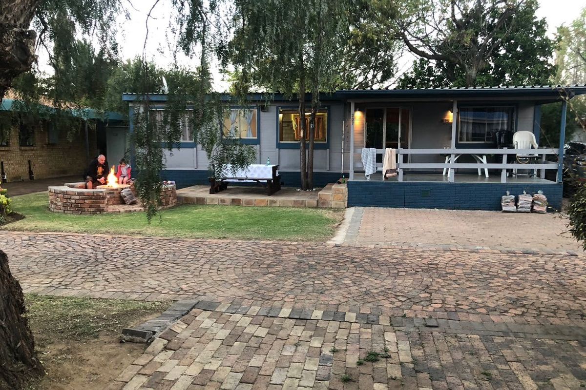Rear view of the property featuring a covered patio, timber decking, and a brick fire pit set within a paved garden area.