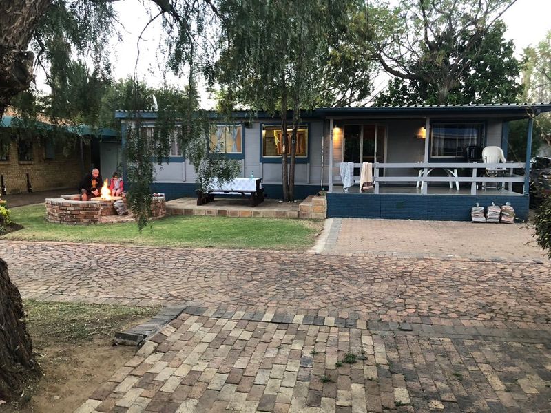 Rear view of the property featuring a covered patio, timber decking, and a brick fire pit set within a paved garden area.