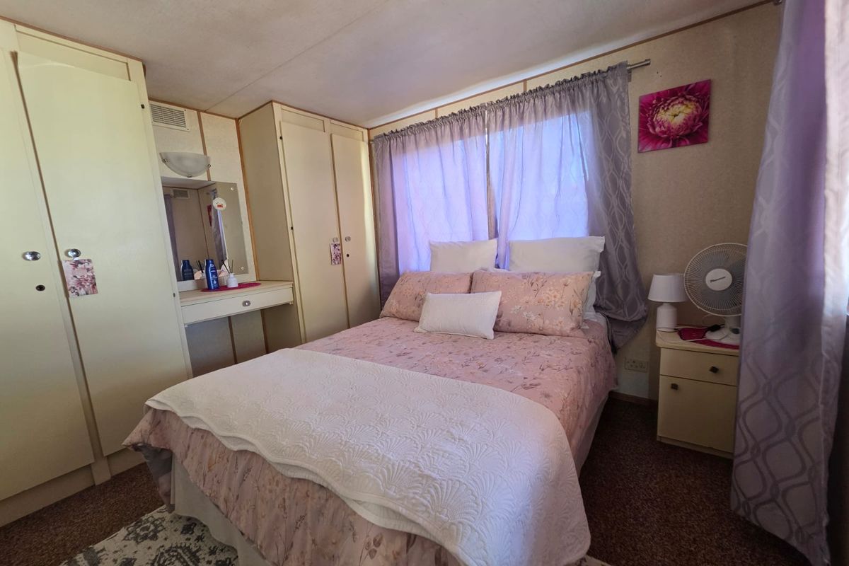 A compact bedroom featuring built-in wardrobes, a vanity unit, and carpeted flooring, offering a functional layout with potential for cosmetic updates.