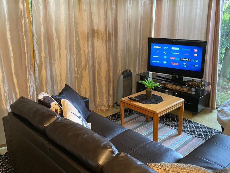 A living room area featuring tiled flooring and large sliding glass doors covered by curtains, providing access to the exterior.