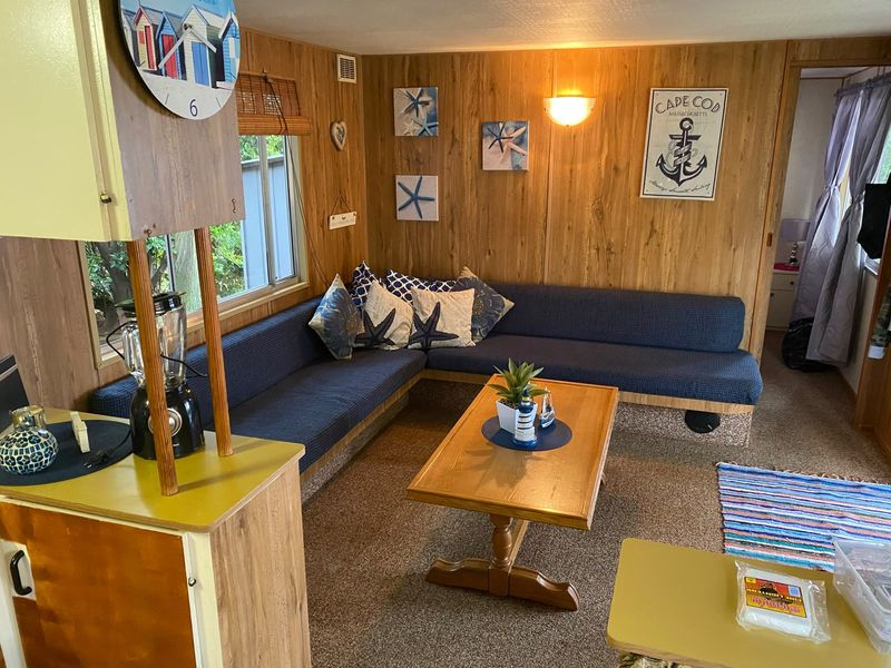 A living room featuring dated wood paneling, built-in corner seating, and carpet flooring, offering a cozy but dated aesthetic ready for modernization.