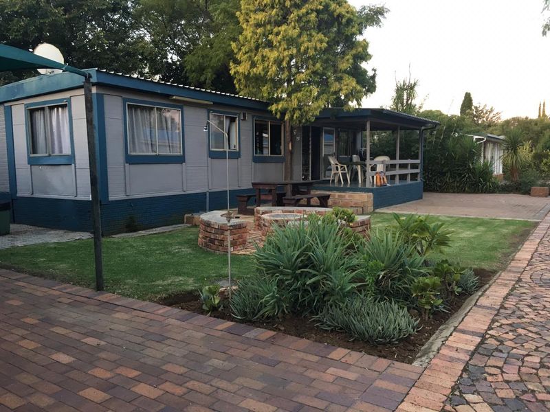 Rear view of the property featuring a covered patio, a brick fire pit, and a well-maintained garden with paved pathways.