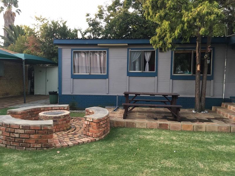 Rear exterior view featuring a brick fire pit, tiled patio area, and a shaded outdoor space adjacent to the main dwelling.