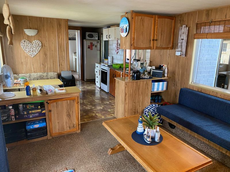 Open plan living and kitchen area featuring dated wood paneling, built-in cabinetry, and a mix of carpet and vinyl flooring.