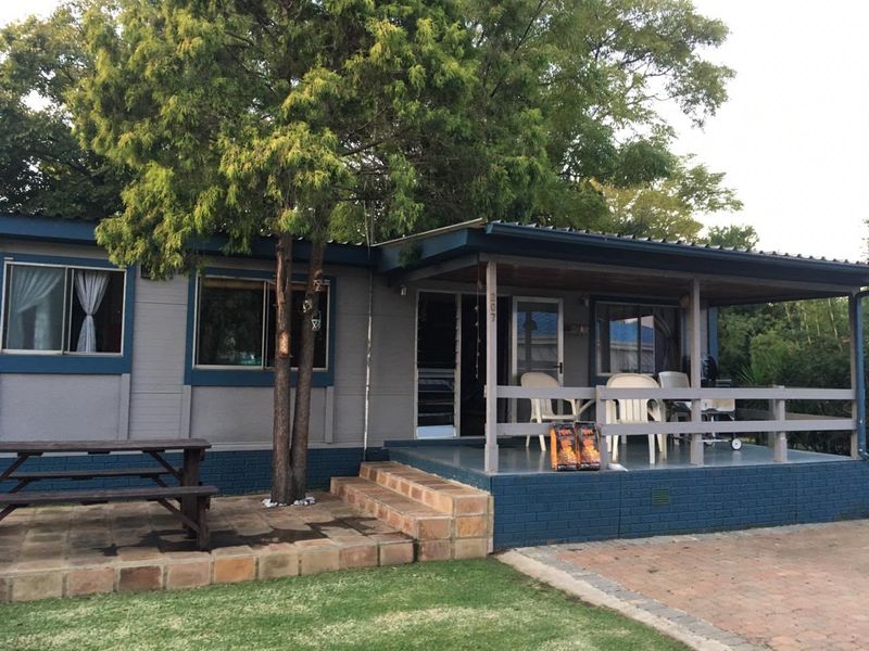 Front view of a single-story home featuring a covered patio, timber decking, and a paved entrance area with established garden surroundings.