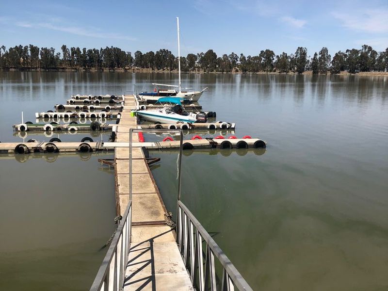 A view of a concrete jetty extending into a calm lake, featuring metal handrails and boat mooring facilities.