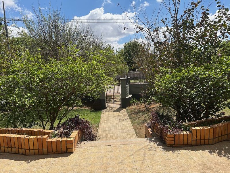 A view from a tiled patio overlooking a garden with a brick paved walkway leading to a metal pedestrian gate.