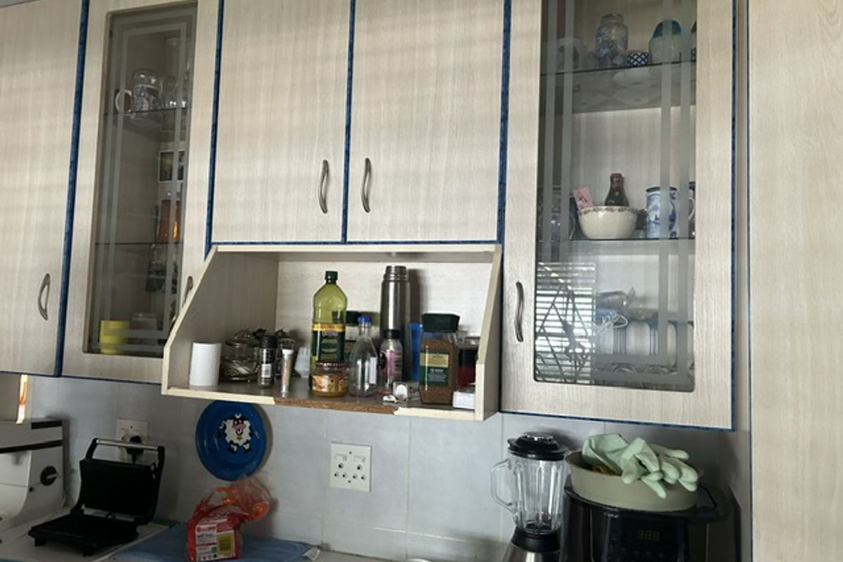 A kitchen area featuring light-toned laminate cabinetry with glass-fronted display sections and a tiled backsplash.