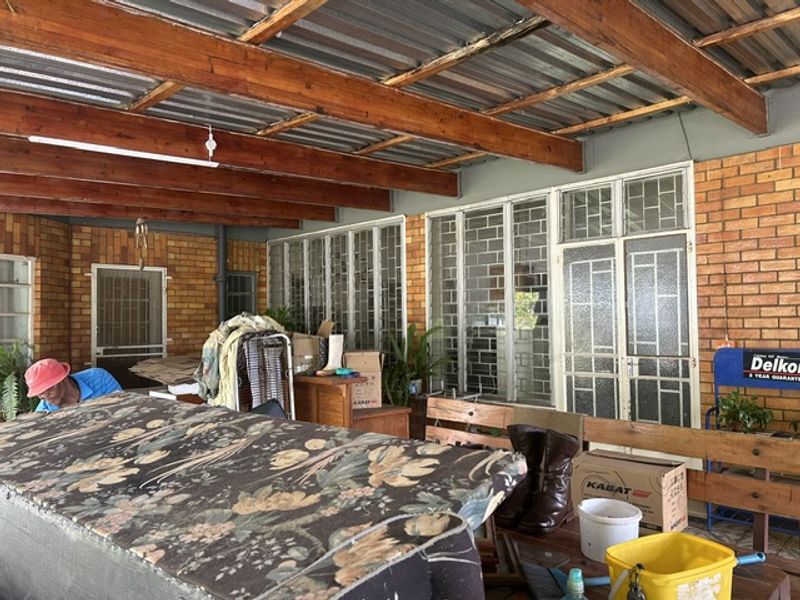 A covered outdoor patio area featuring exposed timber beams, corrugated metal roofing, and face brick walls with security-fitted windows and doors.