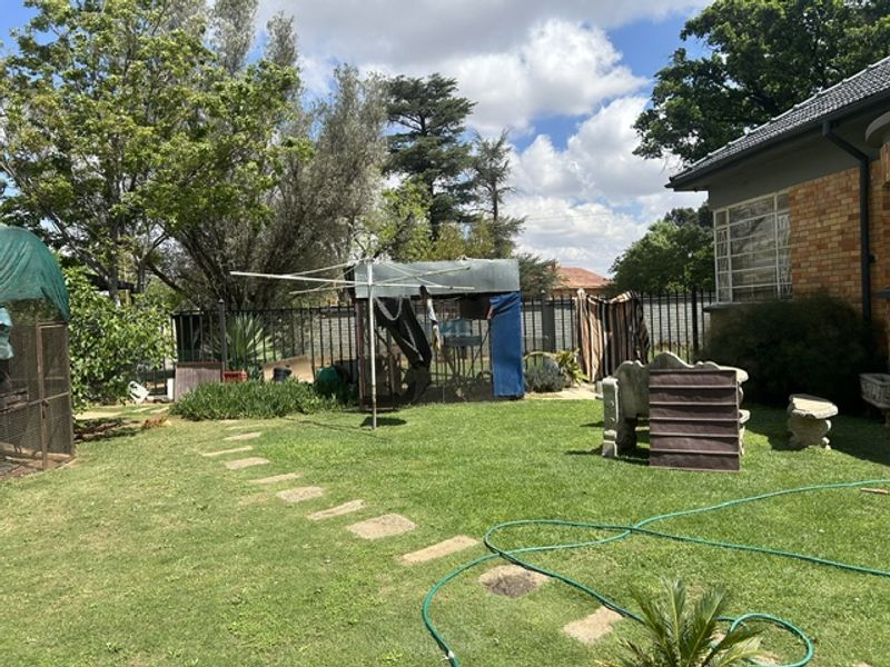 A rear garden view featuring a brick house exterior, established lawn, stone pathway, and perimeter fencing.