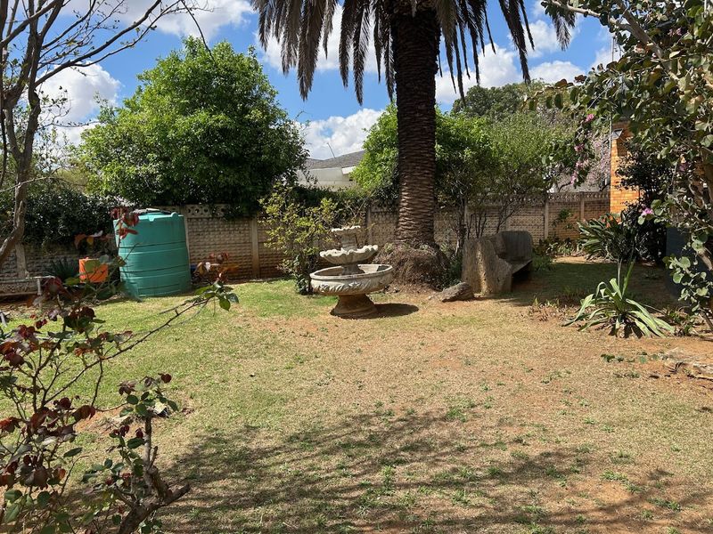 A private garden area featuring a mature palm tree, a stone fountain, and a large water storage tank enclosed by a boundary wall.