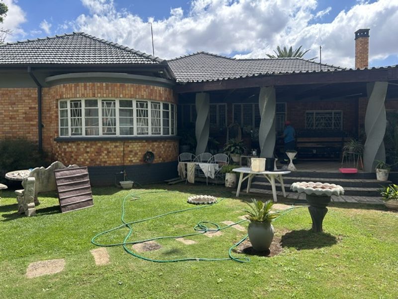 Rear view of a brick house featuring a covered patio with decorative spiral columns, a tiled roof, and a spacious garden area.