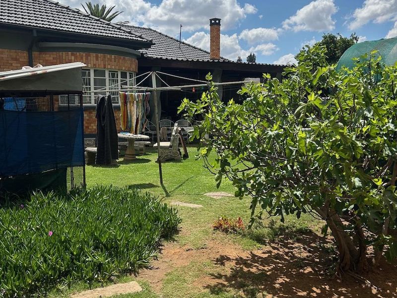 A view of the rear garden featuring a lawn, established trees, and the rear brick facade of the house with a tiled roof and chimney.