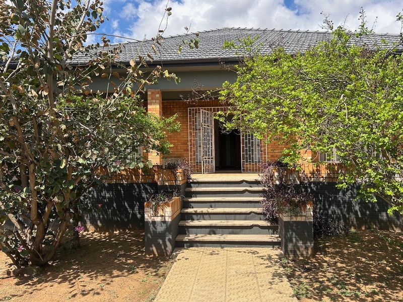 Front elevation of a brick house featuring a covered porch, concrete steps, and a paved walkway leading to the main entrance with security gate.