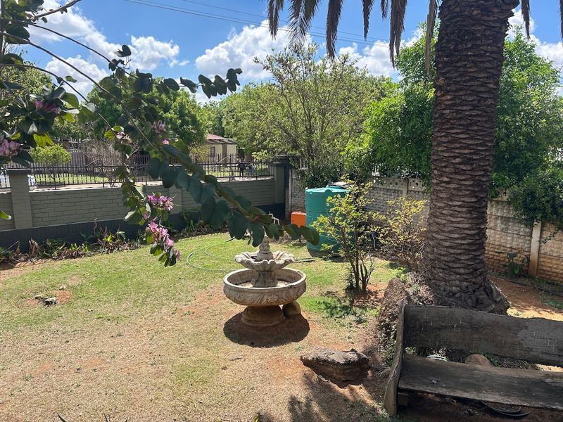 A private garden area featuring a mature palm tree, a stone fountain, and a brick boundary wall with an integrated water tank.