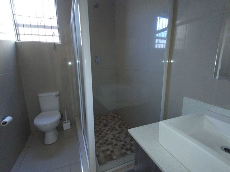 A functional bathroom featuring a glass-enclosed shower, a modern vanity basin, and neutral wall and floor tiling.