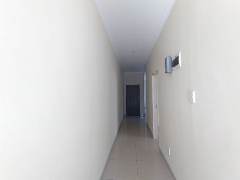 A clean, empty hallway featuring neutral tiled flooring, recessed lighting, and access to adjacent rooms.