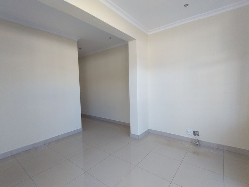 A bright, empty living area featuring neutral tiled flooring, recessed downlighting, and coved cornicing, providing a clean canvas for interior design.