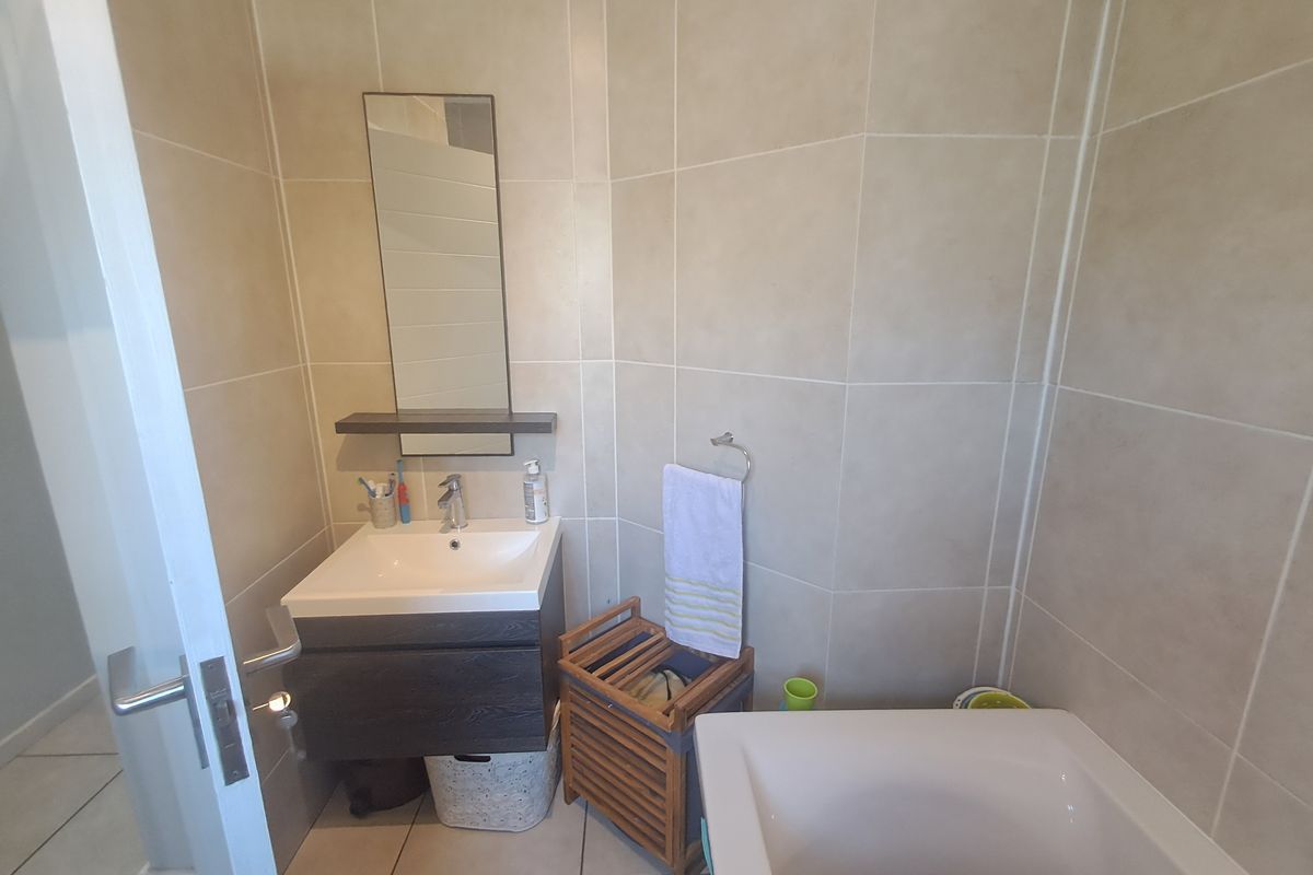 A compact bathroom featuring a wall-mounted vanity with basin, tiled walls, and a bathtub.