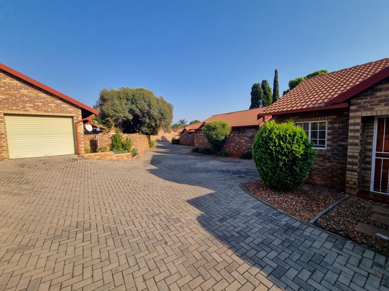 A view of the paved driveway and facebrick townhouse exteriors within a residential complex, featuring tiled roofs and established landscaping.
