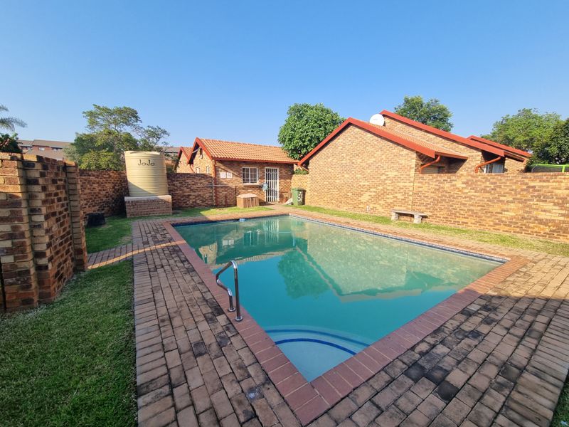 A private outdoor pool area featuring a paved surround, brick boundary walls, and a water storage tank set within a townhouse garden.