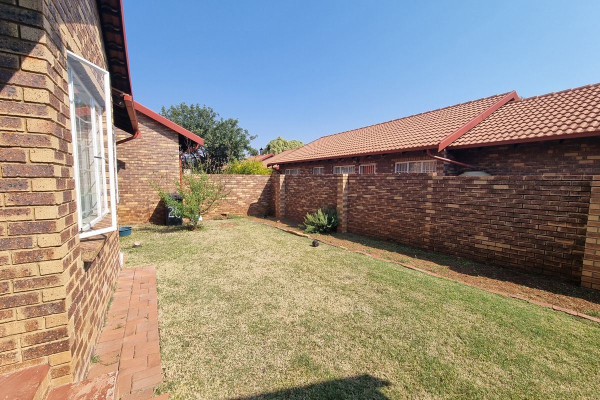 A private rear garden area featuring face brick walls, a tiled roof, and a paved walkway along the side of the townhouse.