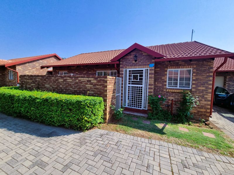 Front exterior view of a brick townhouse featuring a tiled roof, paved driveway, and a secure entrance gate with a private garden area.
