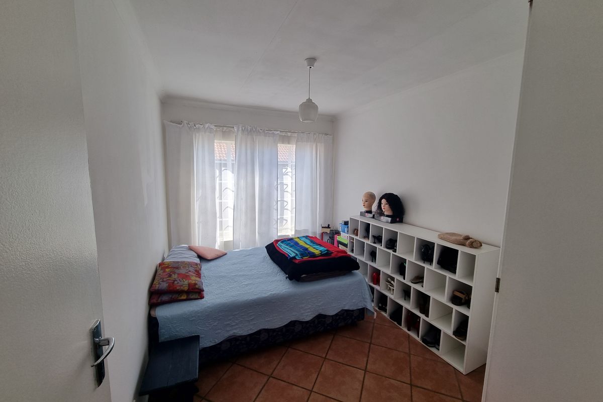 A standard bedroom featuring tiled flooring and a window with security gate, providing a functional space for rest.