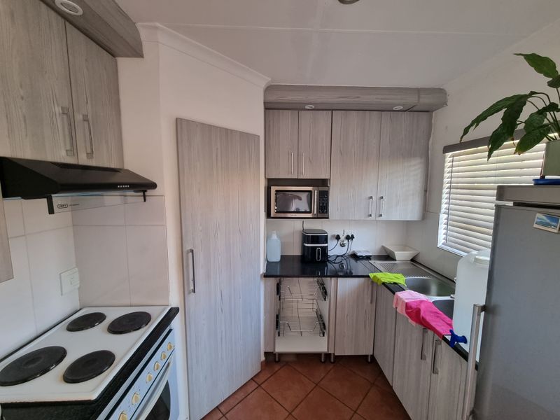 A functional kitchen featuring light wood-grain cabinetry, black countertops, an electric stove with extractor fan, and a stainless steel sink.