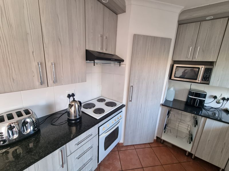 A functional kitchen featuring wood-grain cabinetry, granite countertops, an electric hob with extractor fan, and a built-in oven and microwave.