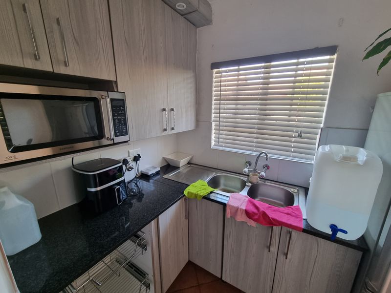 A functional kitchen area featuring granite countertops, double stainless steel sink, built-in microwave, and light wood-grain cabinetry with ample storage space.