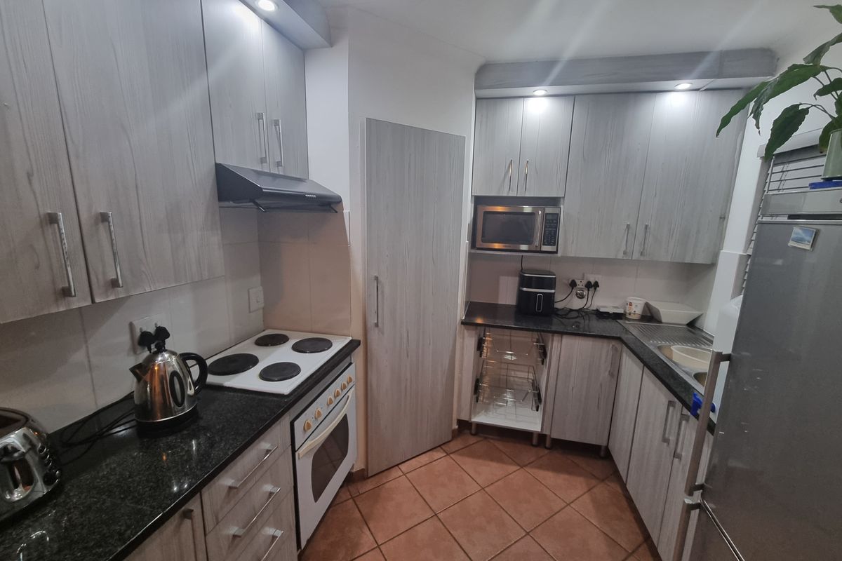 A functional kitchen featuring light wood-grain cabinetry, granite countertops, built-in oven and hob, and tiled flooring with ample storage space.