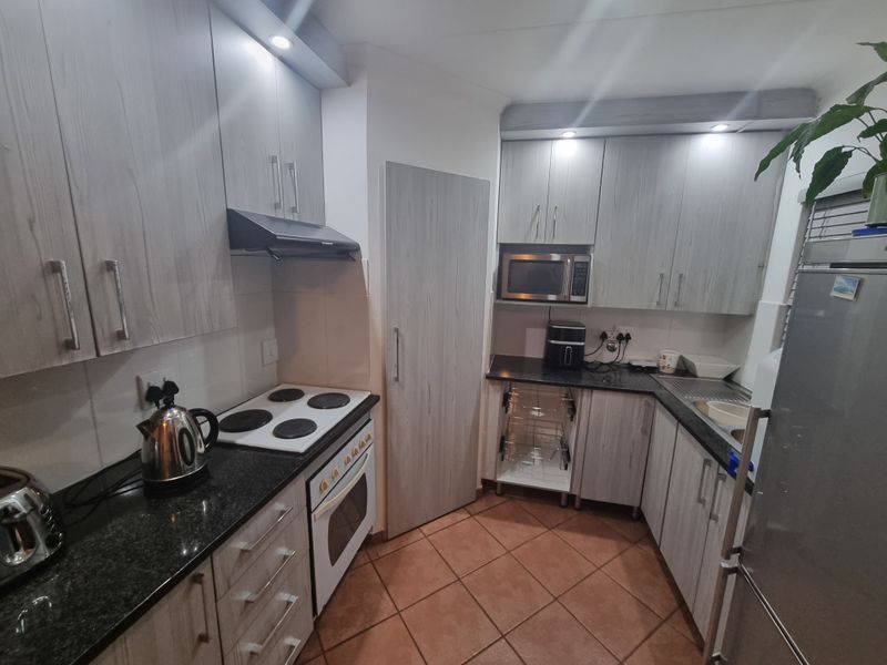 A functional kitchen featuring light wood-grain cabinetry, granite countertops, built-in oven and hob, and tiled flooring with ample storage space.