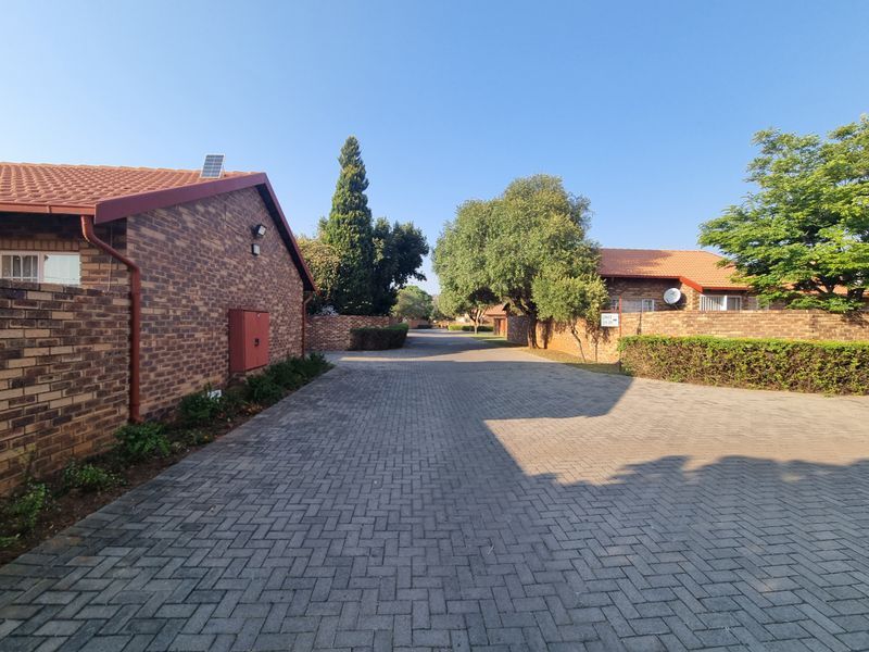 A view of the paved driveway and access road within the townhouse complex, featuring facebrick exterior walls and established landscaping.