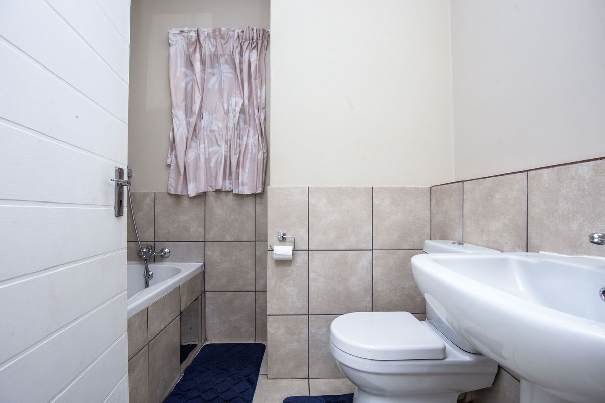 A functional bathroom featuring a bathtub, pedestal basin, and toilet with neutral wall and floor tiling.