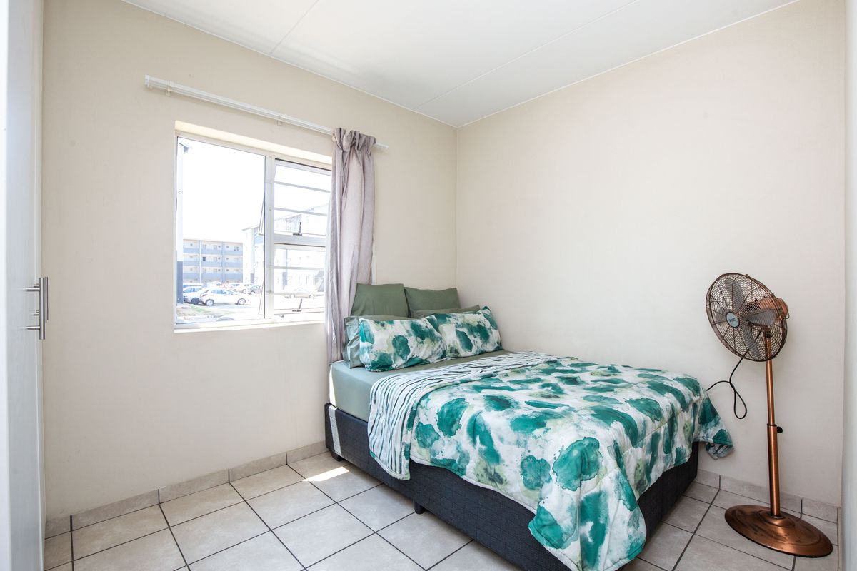 A functional bedroom featuring tiled flooring, a built-in cupboard, and a window providing natural light.