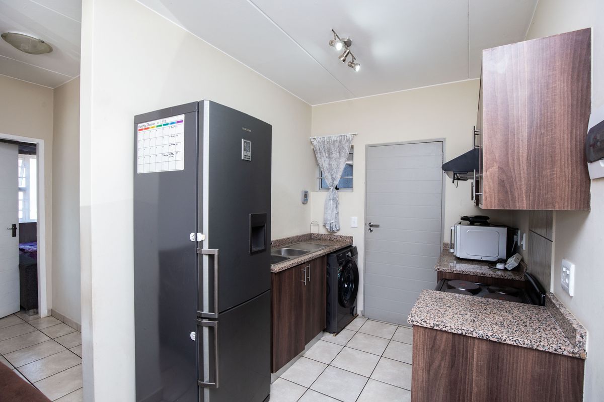 Functional kitchen featuring granite countertops, dark wood cabinetry, built-in oven and hob, and tiled flooring with integrated laundry appliance space.