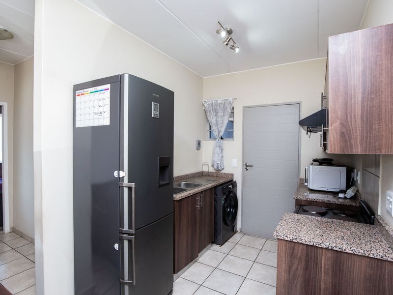 Functional kitchen featuring granite countertops, dark wood cabinetry, built-in oven and hob, and tiled flooring with integrated laundry appliance space.