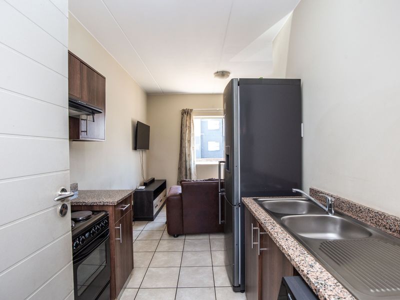 Compact open-plan kitchen featuring granite countertops, double stainless steel sink, and dark wood cabinetry, flowing into a small living area.