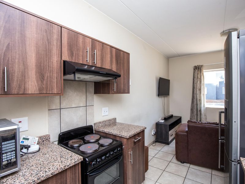 Open plan kitchen and living area featuring wood-look cabinetry, granite countertops, electric stove, and tiled flooring throughout.