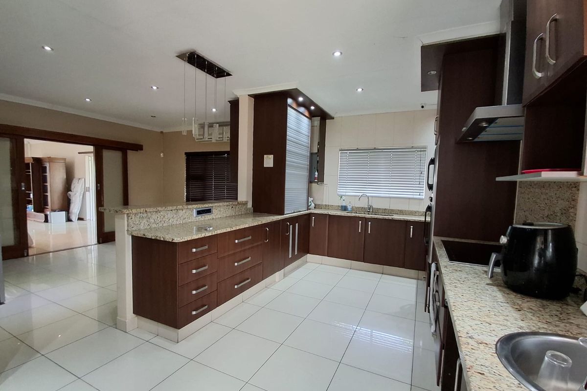Modern kitchen featuring dark wood cabinetry, granite countertops, tiled flooring, and recessed lighting, with an open-plan layout connecting to the adjacent living area.
