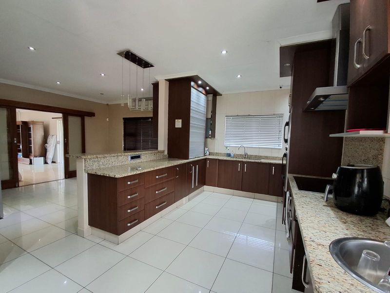 Modern kitchen featuring dark wood cabinetry, granite countertops, tiled flooring, and recessed lighting, with an open-plan layout connecting to the adjacent living area.