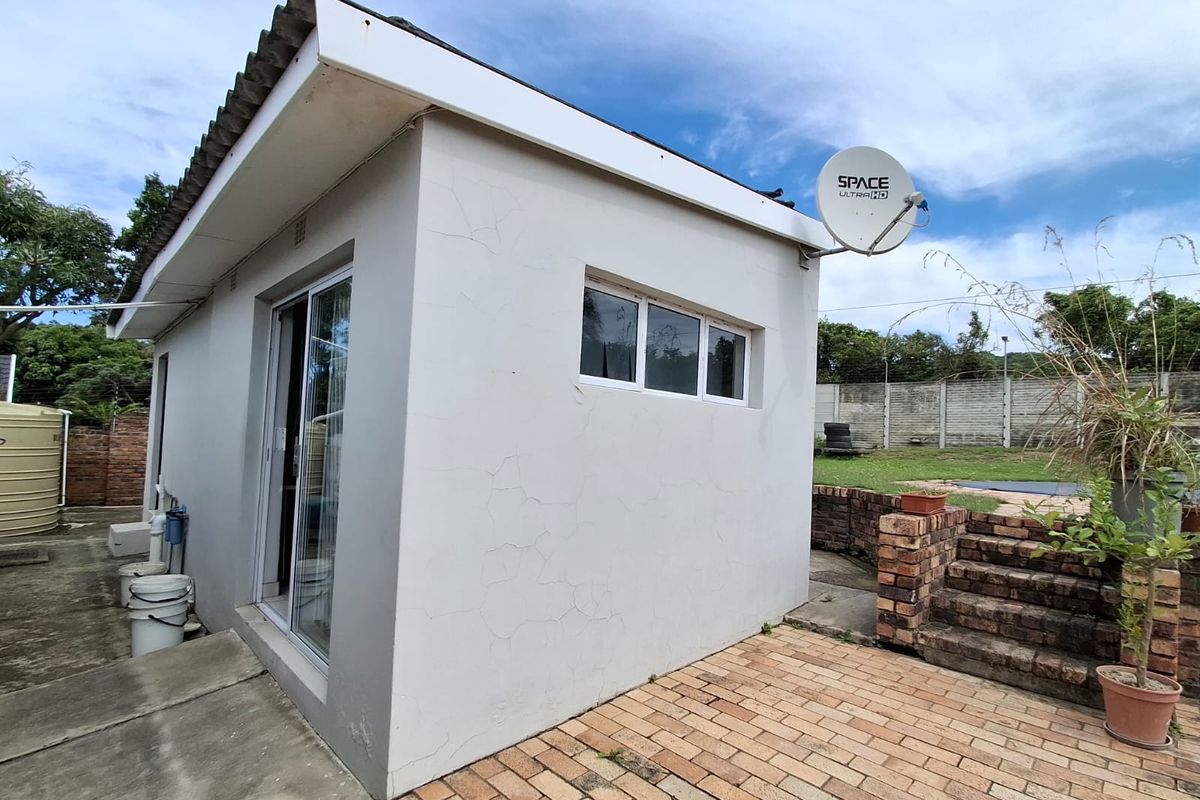Rear exterior view of the property featuring a small outbuilding with sliding glass doors, brick paving, and a satellite dish installation.