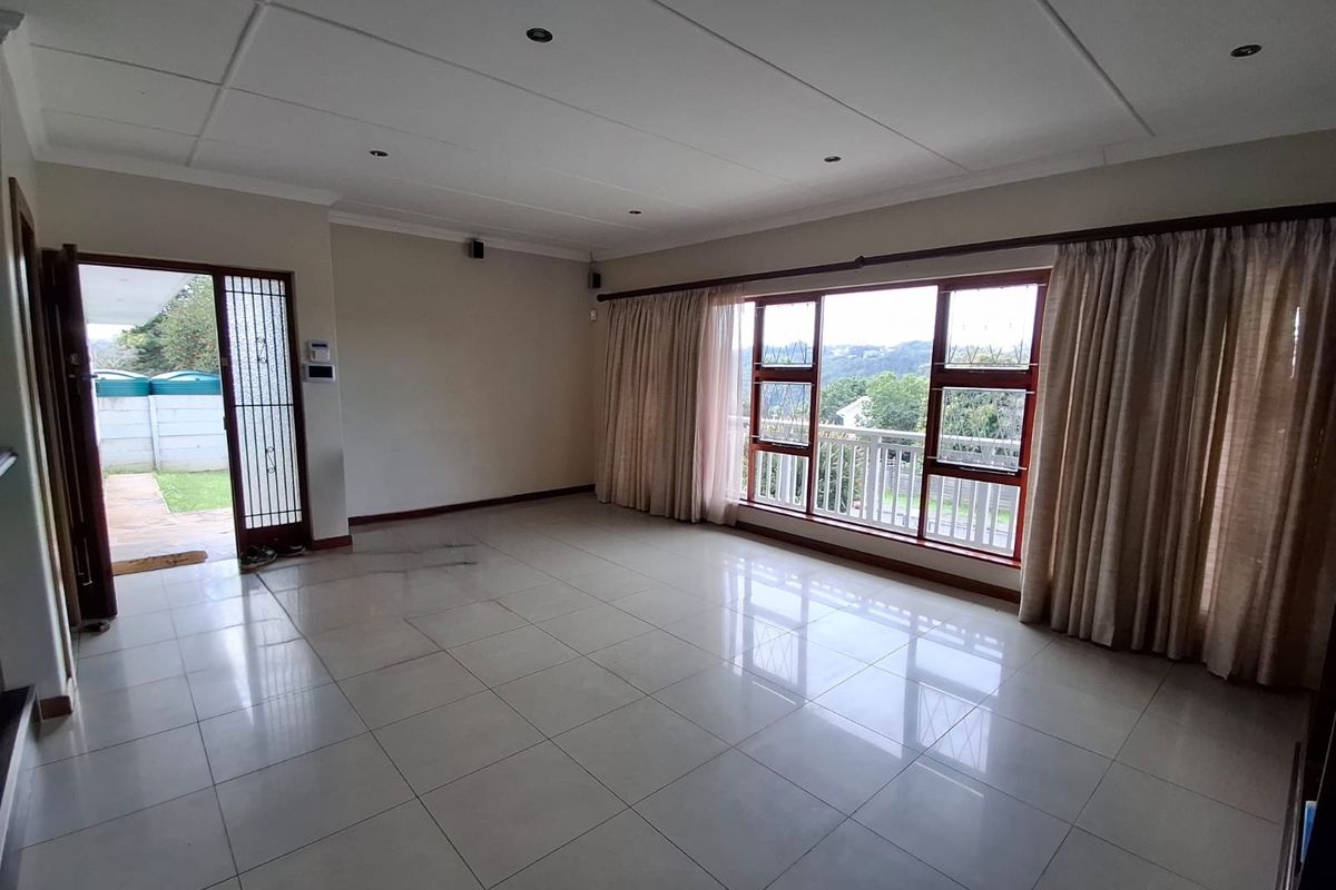 Spacious, empty living room featuring large windows with natural light, tiled flooring, and direct access to an outdoor area through a security gate.