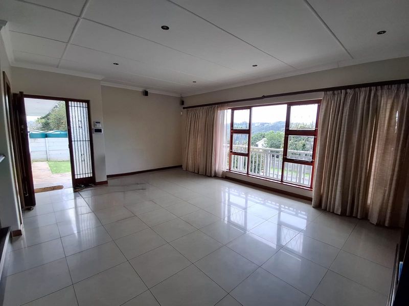 Spacious, empty living room featuring large windows with natural light, tiled flooring, and direct access to an outdoor area through a security gate.