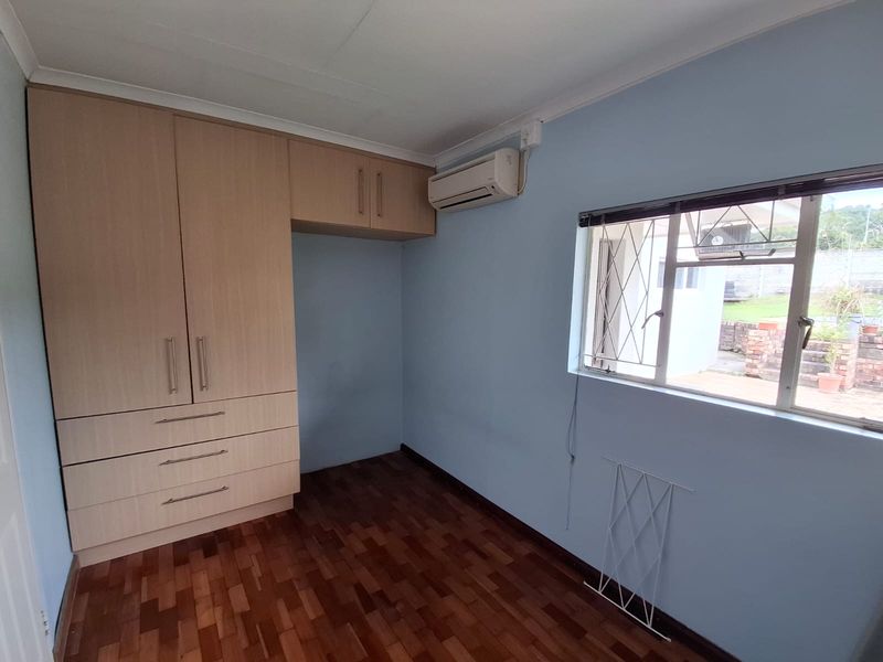 A bright bedroom featuring parquet flooring, built-in wooden cupboards, and a wall-mounted air conditioning unit.